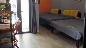 Ένα μοντέρνο δωμάτιο με έναν καναπέ, ένα κρεβάτι με κίτρινα μαξιλάρια, ένα τραπέζι φαγητού με καρέκλες και ένα ράφι με διάφορα αντικείμενα.