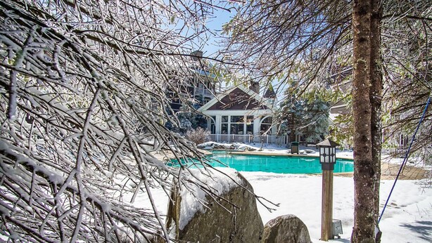 A snow-covered landscape with a pool, a house with a balcony, and a wooden post with a lantern. - Allegheny Springs 414: Junior Studio Slopeside (Snowshoe)
