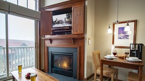 A cozy room with a fireplace, a dining table with chairs, a coffee maker, and a television mounted on a wooden cabinet. - Allegheny Springs 414: Junior Studio Slopeside (Snowshoe)