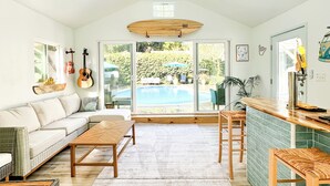 Un salón amplio con un ventilador de techo grande, una mesa de comedor de madera, un sofá y vistas a una piscina a través de grandes ventanales.