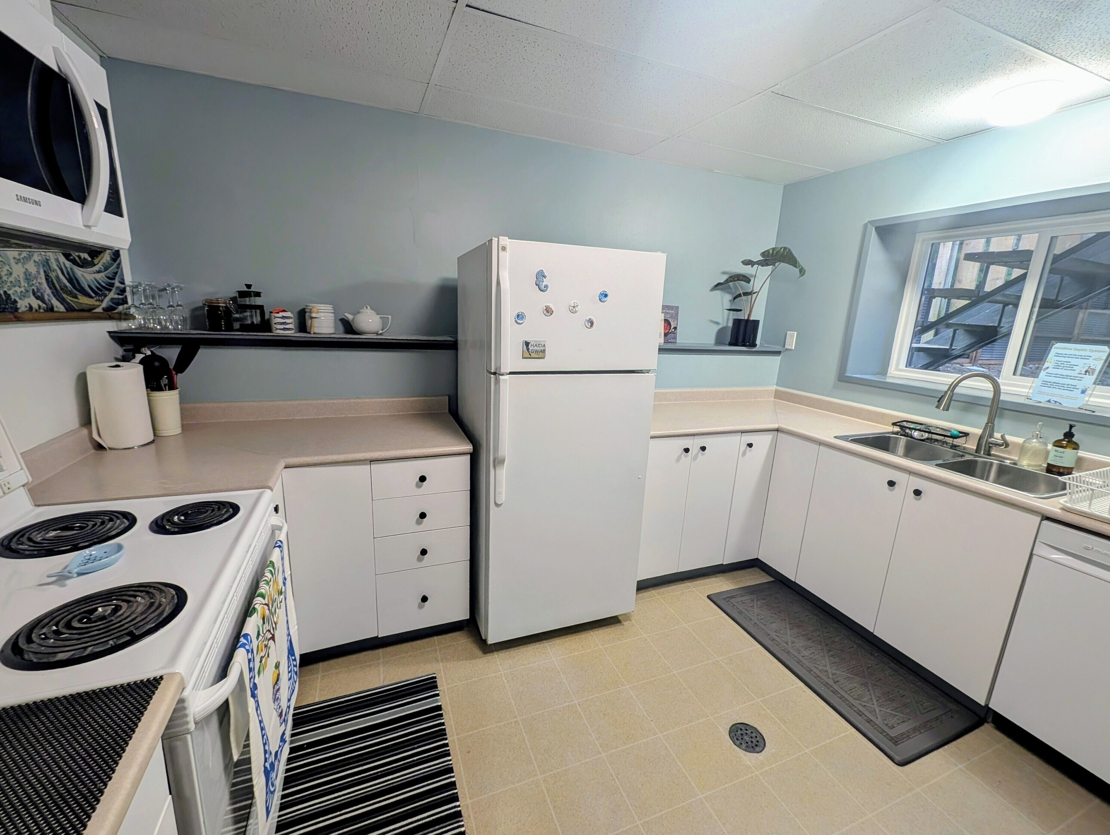 A kitchen with a white refrigerator, stove, and cabinets. There is a window with a view of the outside.