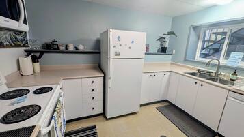 A kitchen with a white refrigerator, stove, and cabinets. There is a window with a view of the outside.