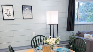 A dining area with a round table set for four, surrounded by green chairs. There is a vase with white flowers on the table, and a tall floor lamp with a white shade is positioned behind the table. - Comfortable Home in the Comox Valley (Comox)