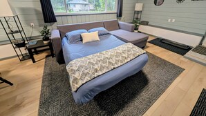 A bedroom with a bed, a sofa, a small table, a plant, and a window with curtains. - Comfortable Home in the Comox Valley (Comox)