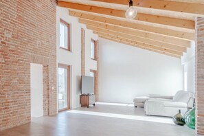 Una habitación amplia con paredes de ladrillo visto, un sofá blanco, un televisor de pantalla plana y una lámpara colgante.