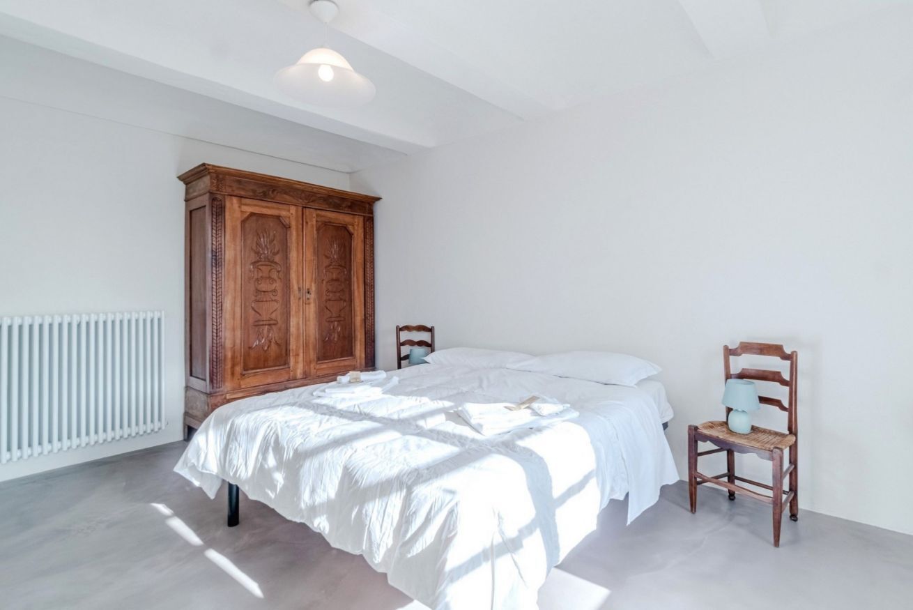 Un dormitorio con cama, armario de madera, silla y radiador.