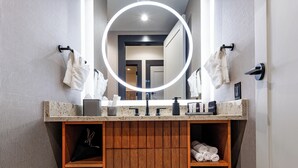 Un baño con tocador de madera, un espejo con luz y toallas en estantes.