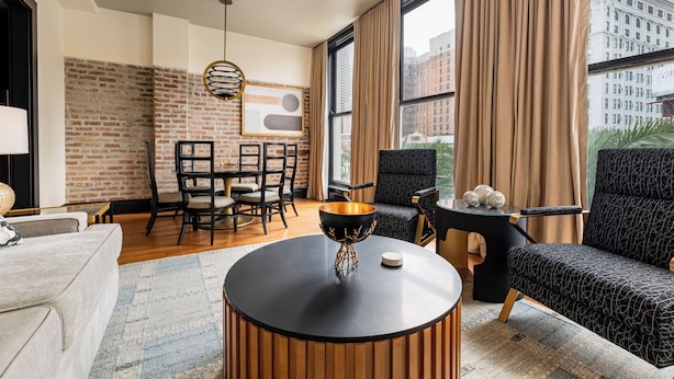 Un salon moderne avec un mur en briques, une table basse ronde en bois, un canapé noir et un coin repas comprenant une table et des chaises.