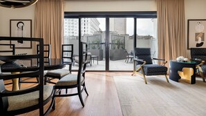 A modern living room with a large sliding glass door leading to an outdoor terrace. The room features a black-framed sofa, a dining table with chairs, and a unique black and gold chandelier.