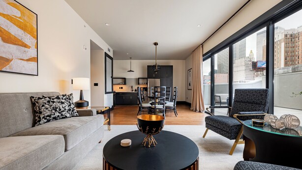 Una sala de estar moderna con un sofá, una mesa de centro y vistas de la ciudad a través de amplias ventanas.