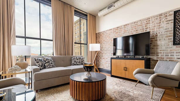 A modern living room with a sofa, armchair, coffee table, and a TV mounted on a brick wall.