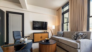 A modern living room with a sofa, armchair, and coffee table, a television mounted on the wall, and a large window with curtains.
