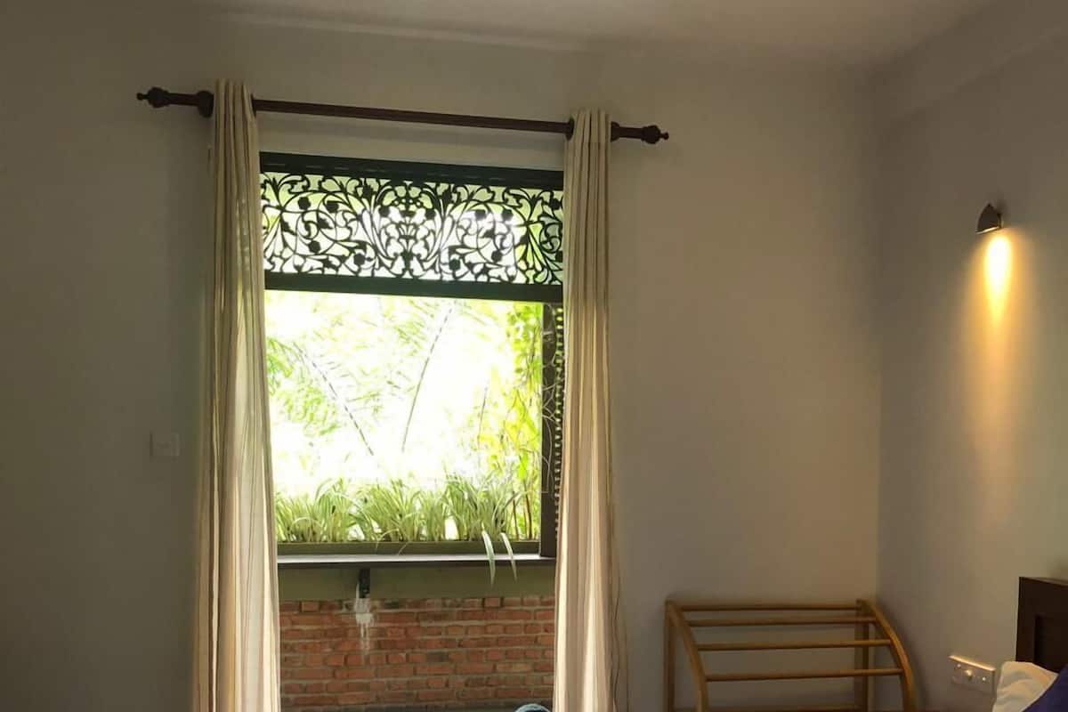 A bedroom with a bed, a chair, a window with curtains, and a ceiling fan.