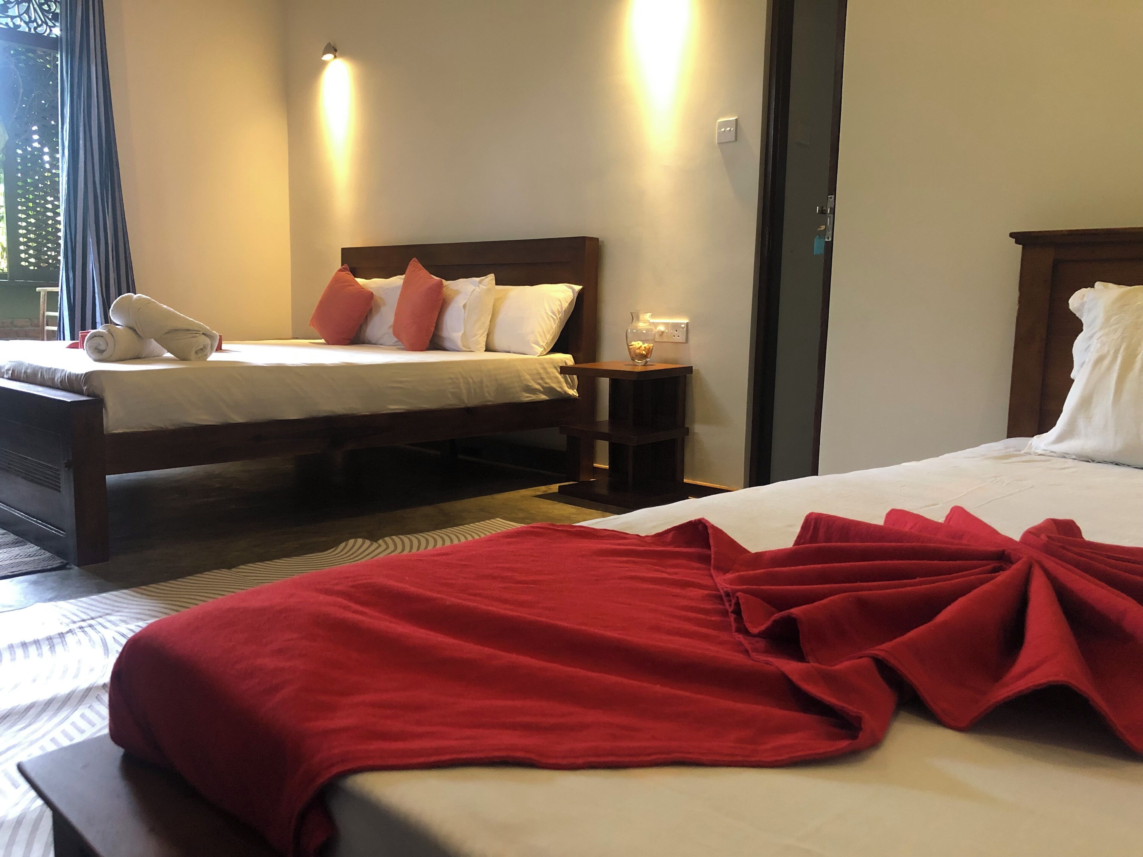 A hotel room with a large bed, a smaller bed, a nightstand with a lamp, and a window with curtains.