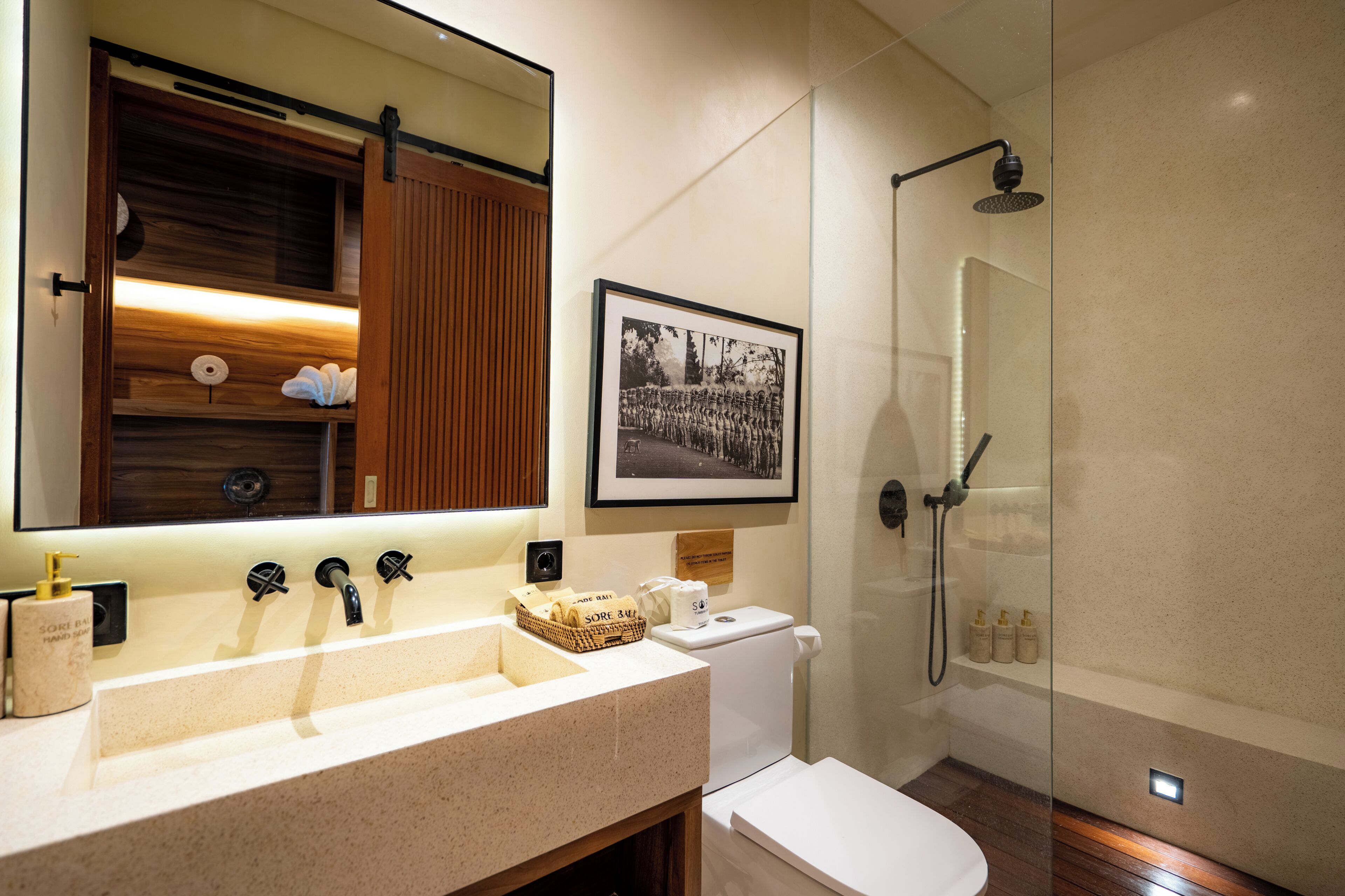 A modern bathroom with a large mirror, a sink with three faucets, a toilet, and a glass-enclosed shower area.