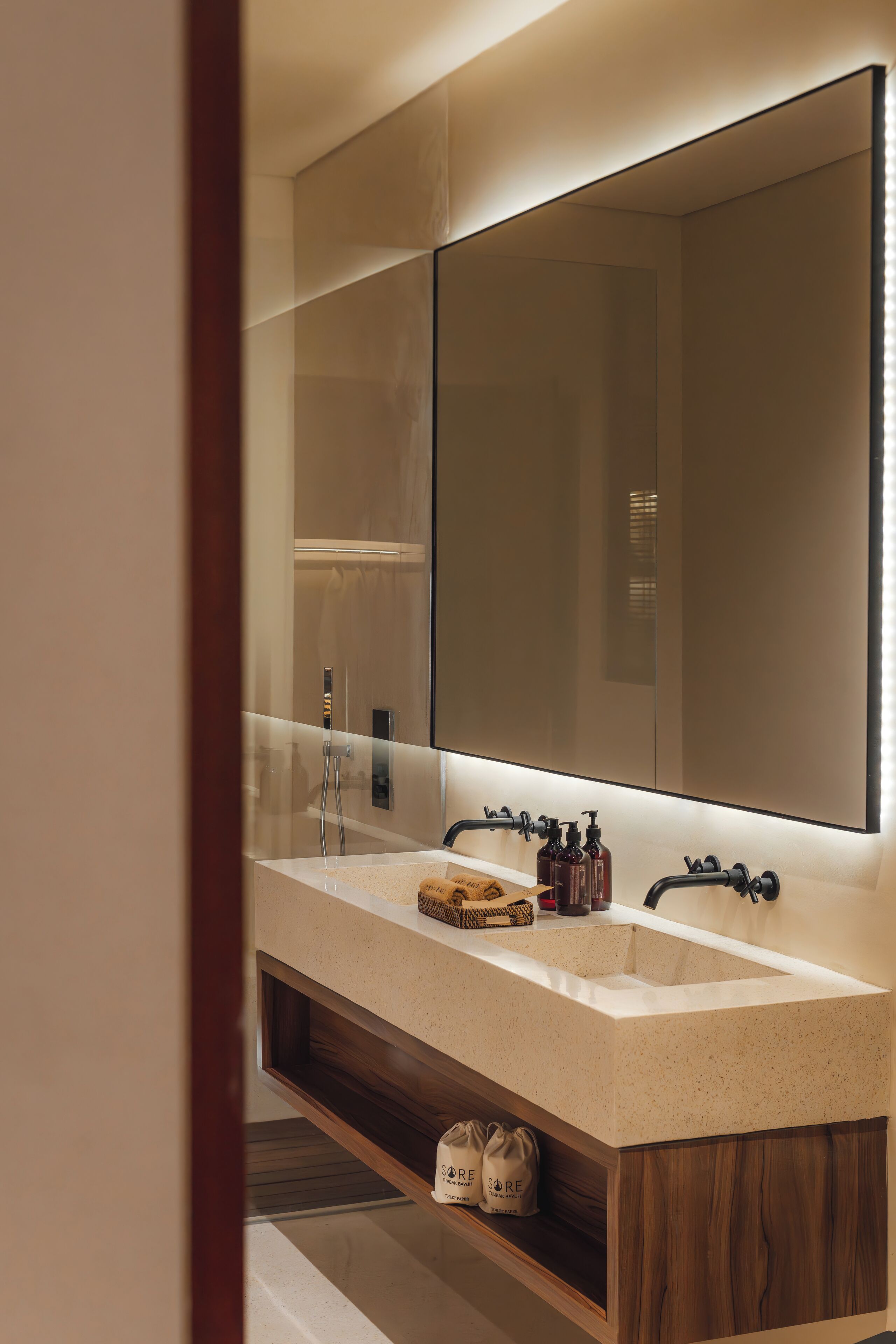Une salle de bain moderne avec un double vasque, un grand miroir et une étagère en bois où sont rangés les produits de toilette.