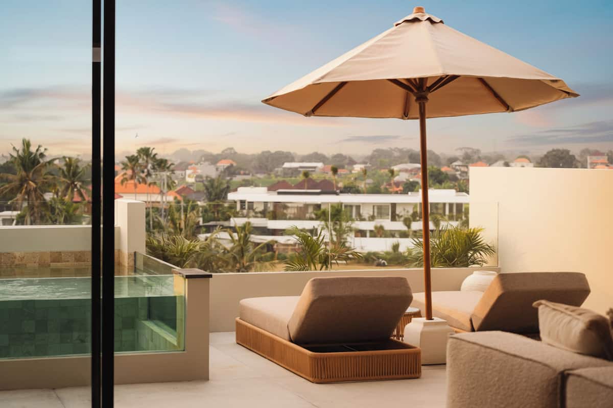 Ein Balkon mit Glasveranda, Liegestuhl, gepolstertem Sitzbrett und Sonnenschirm.