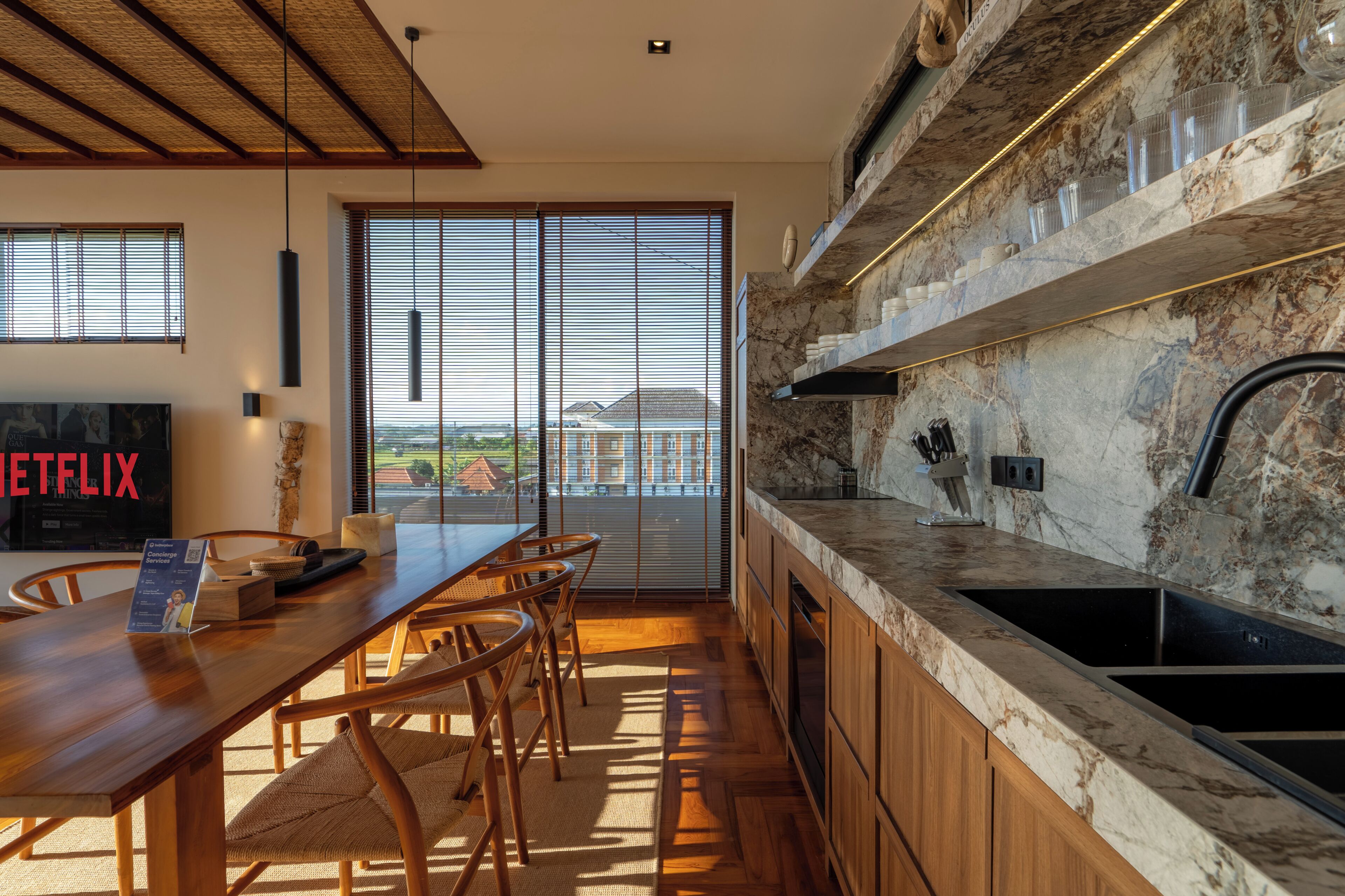 A modern kitchen with a large island, a dining area with chairs, and a view through large windows.