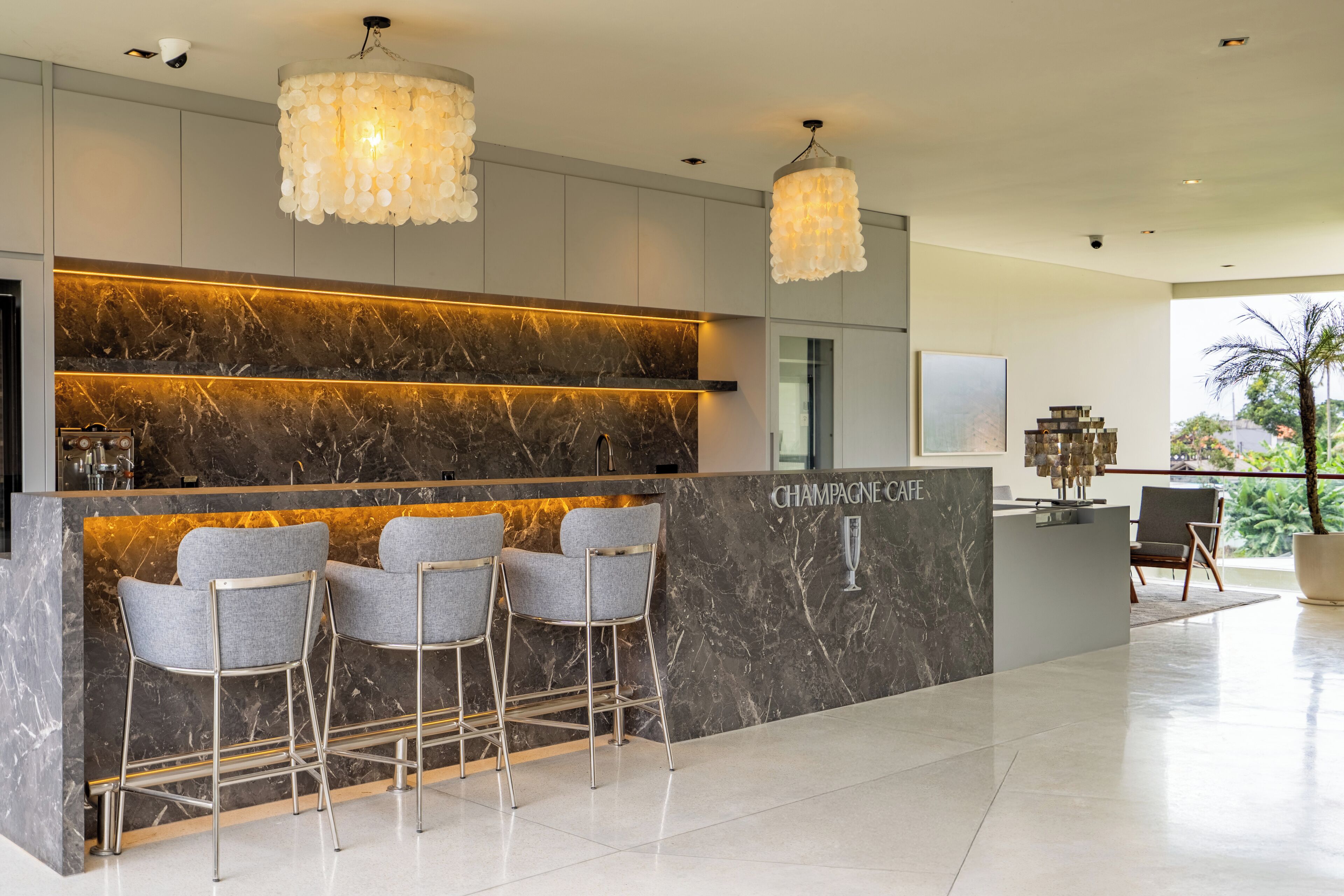 A modern bar area with marble countertops, three grey bar stools, and a 'Champagne Cafe' sign.