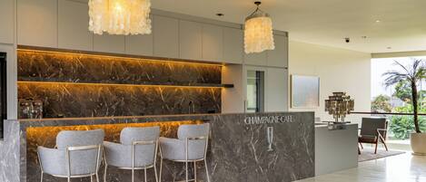 A modern bar area with marble countertops, three grey bar stools, and a 'Champagne Cafe' sign.