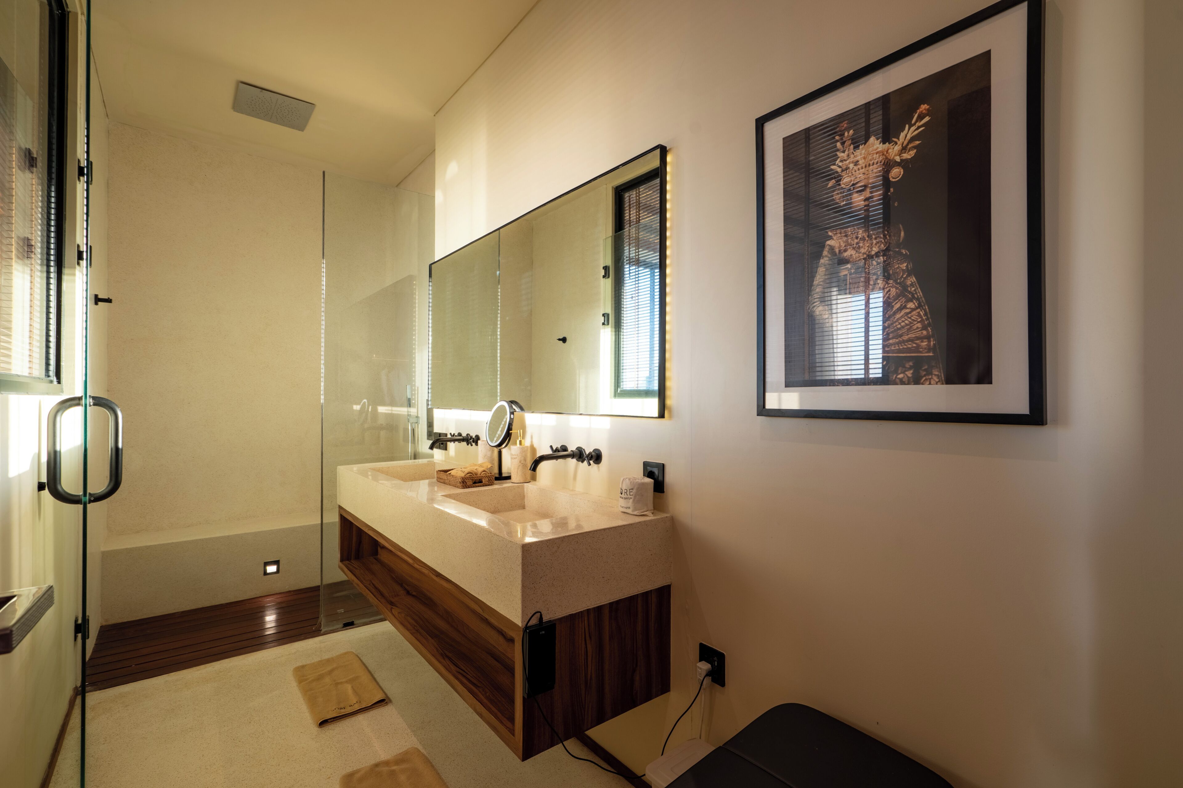 A modern bathroom with a glass shower enclosure, a double sink vanity, and a framed artwork on the wall.