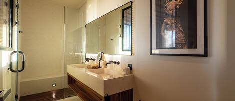 A modern bathroom with a glass shower enclosure, a double sink vanity, and a framed artwork on the wall.
