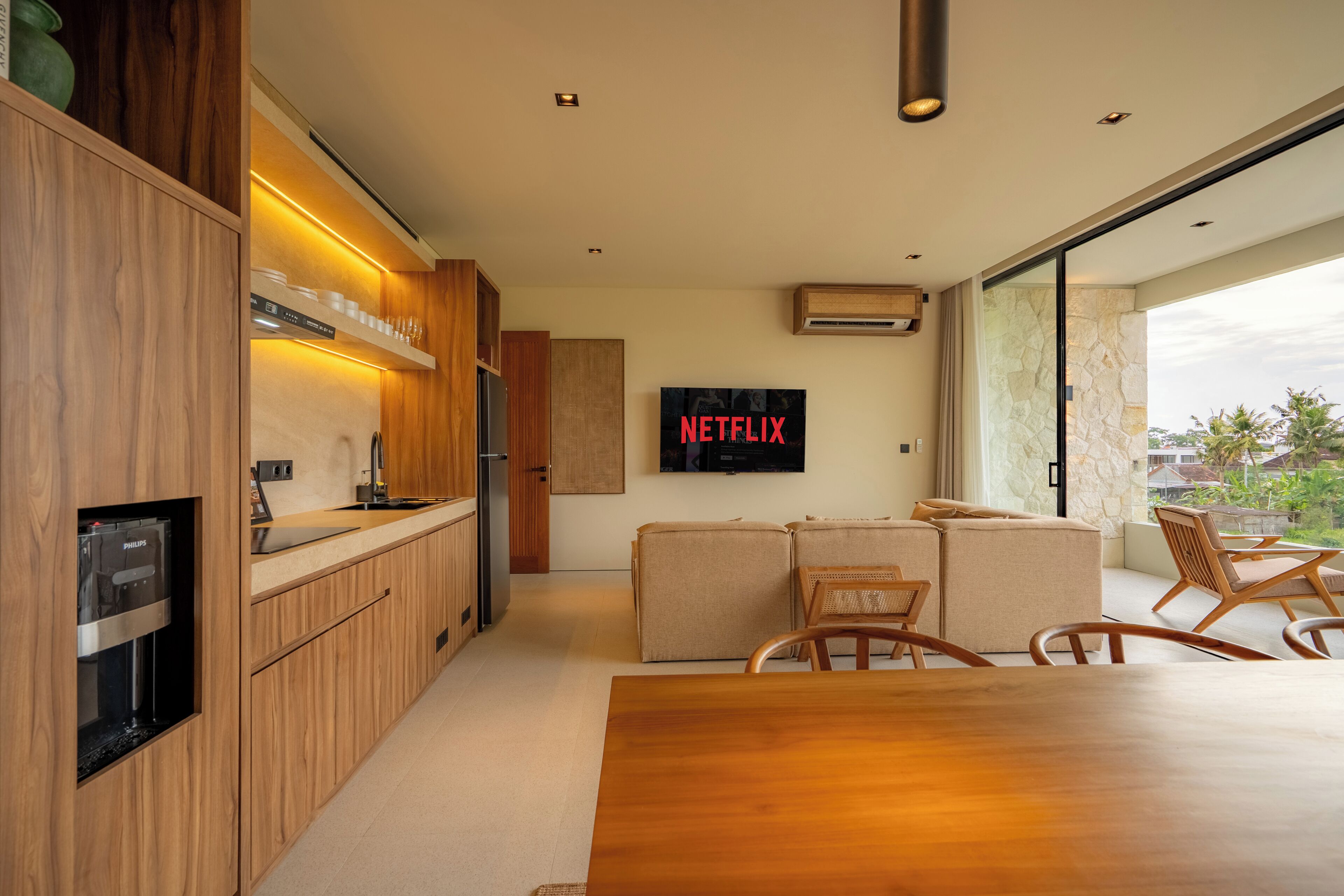Una cocina moderna con armarios de madera, una cafetera integrada y un televisor de pantalla plana mostrando 'NETFLIX'.