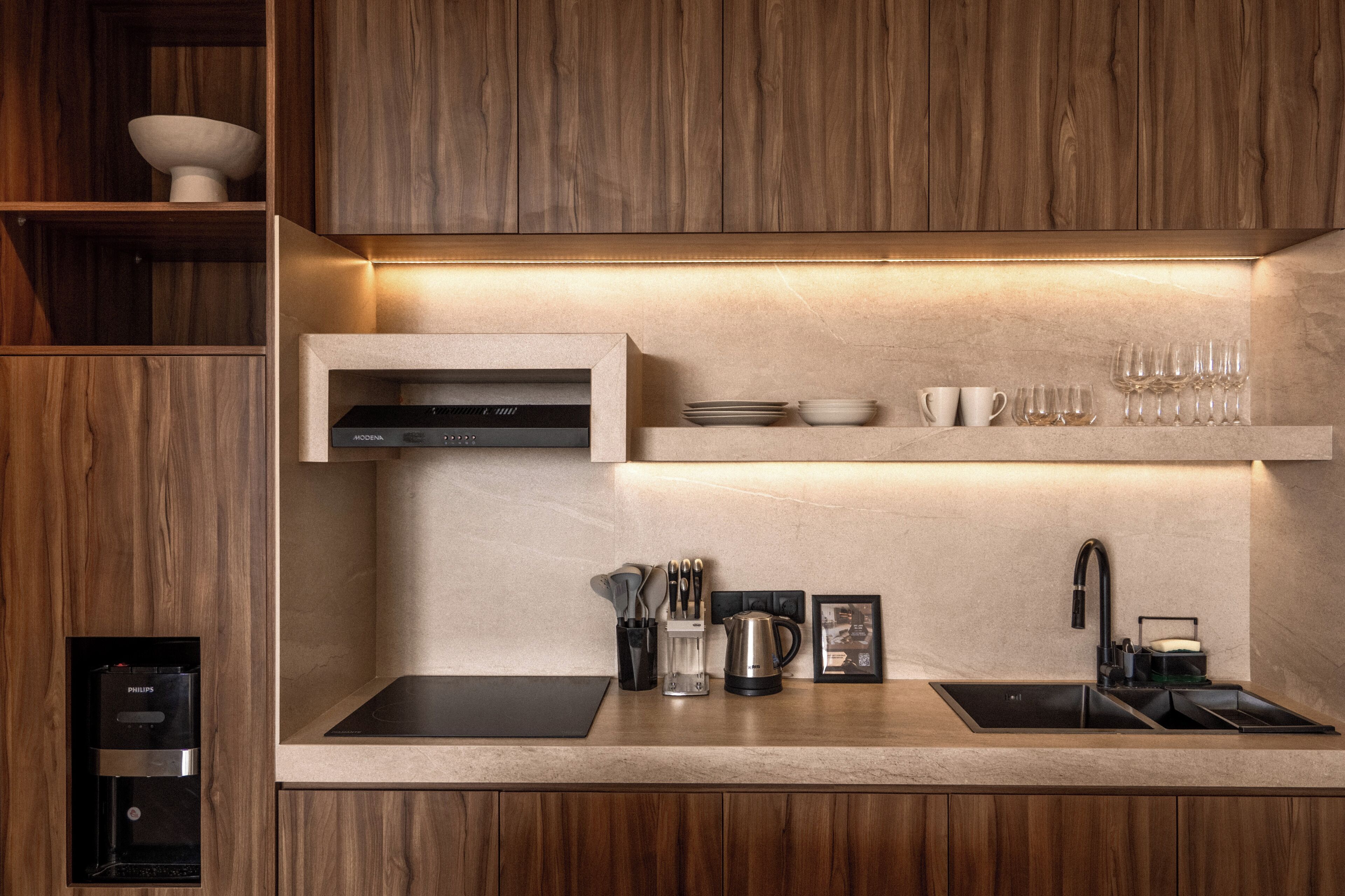 A modern kitchen with wooden cabinetry, a built-in oven, a double sink, and a coffee machine.