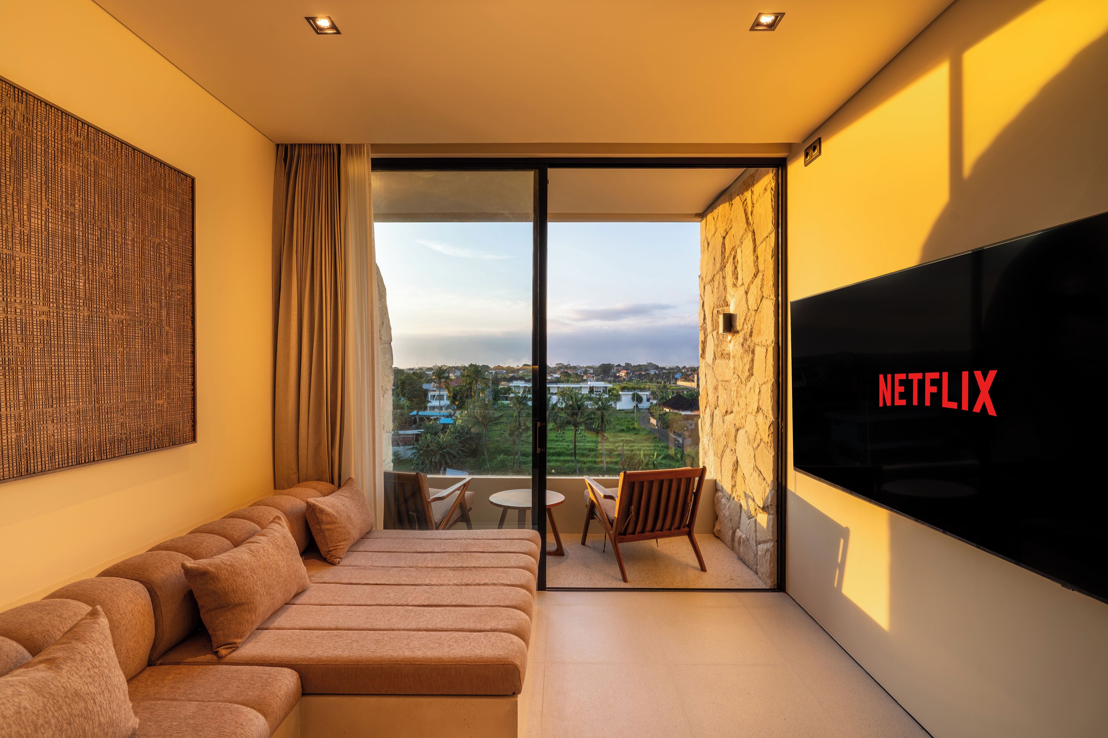 A modern living room with a sofa, a TV, and a balcony with a view of the city.