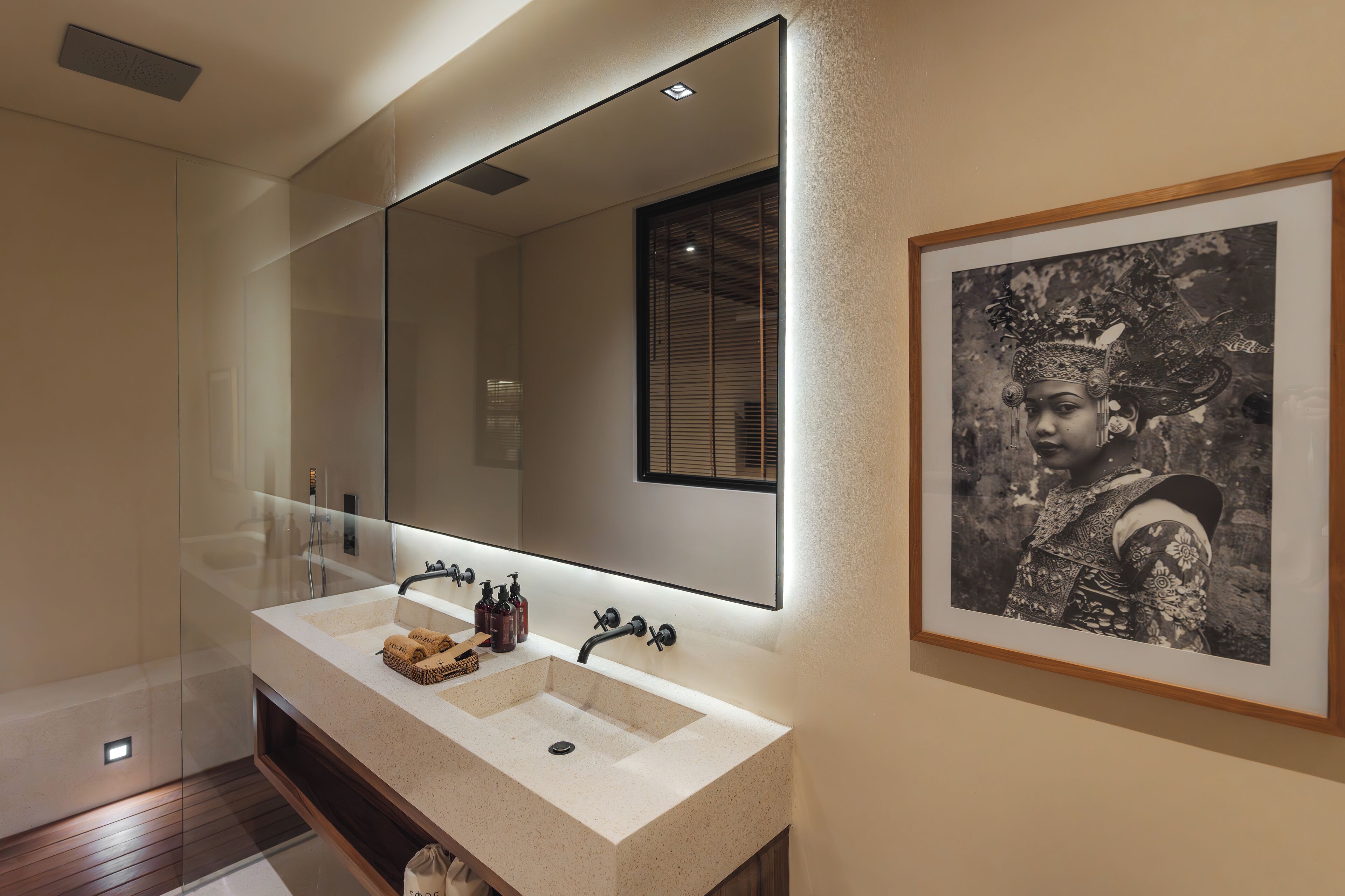 A modern bathroom with a large mirror, a sink with two basins, and a framed black and white photograph on the wall.