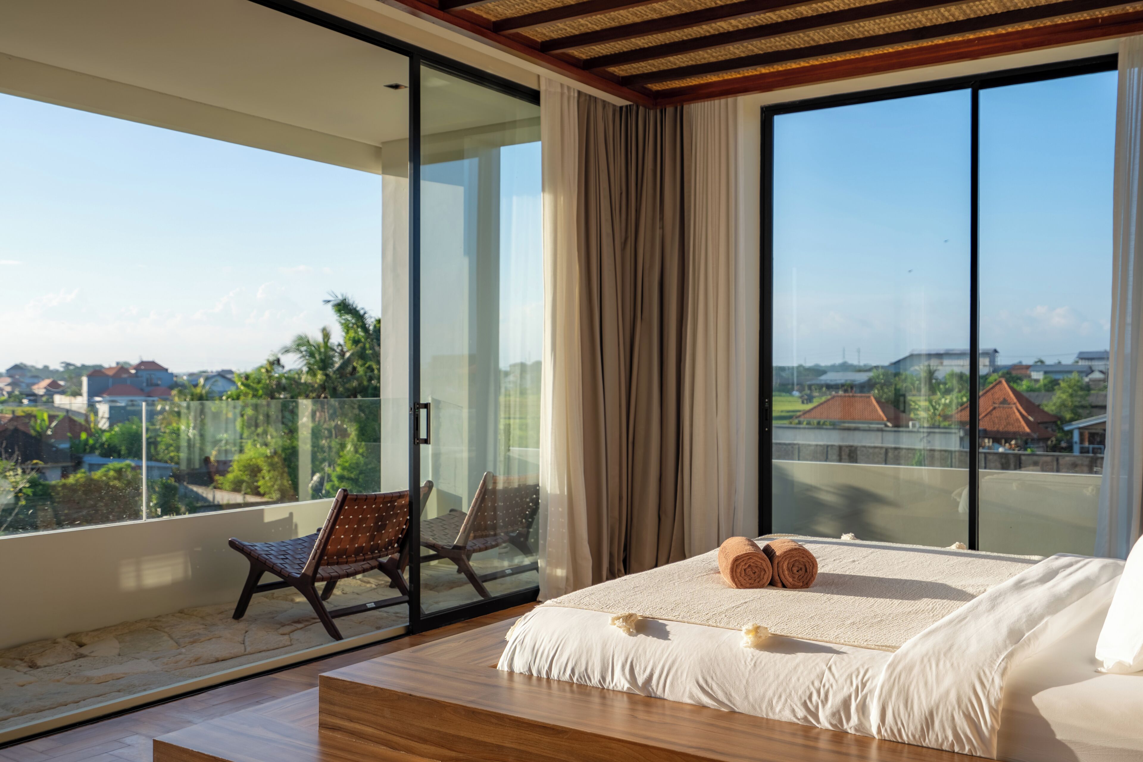 A bedroom with a large bed, a bench, and a chair by a sliding glass door.