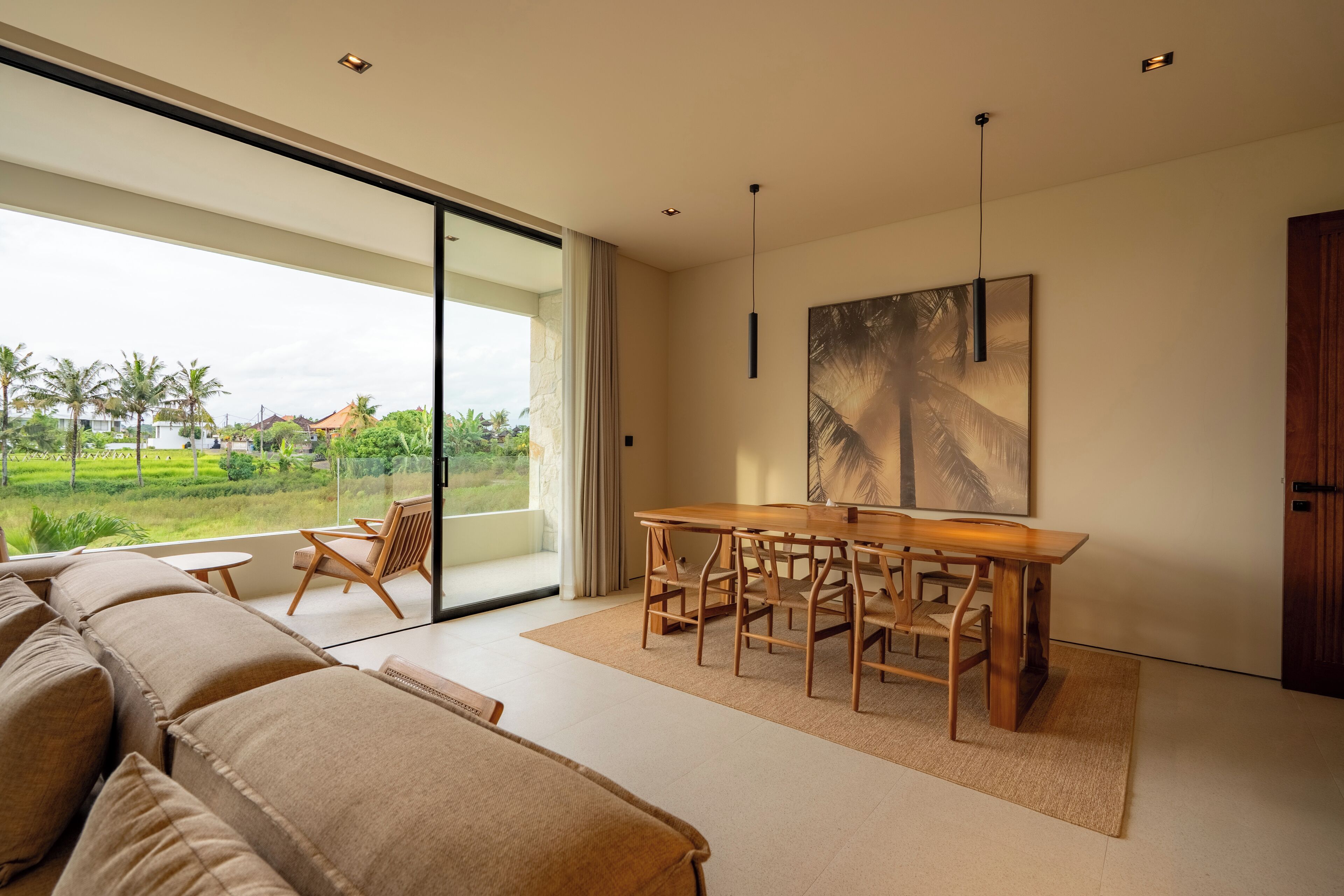Uma sala de estar moderna com uma grande porta de vidro deslizante dando para uma varanda, uma mesa de jantar de madeira com cadeiras e um grande quadro abstrato na parede.