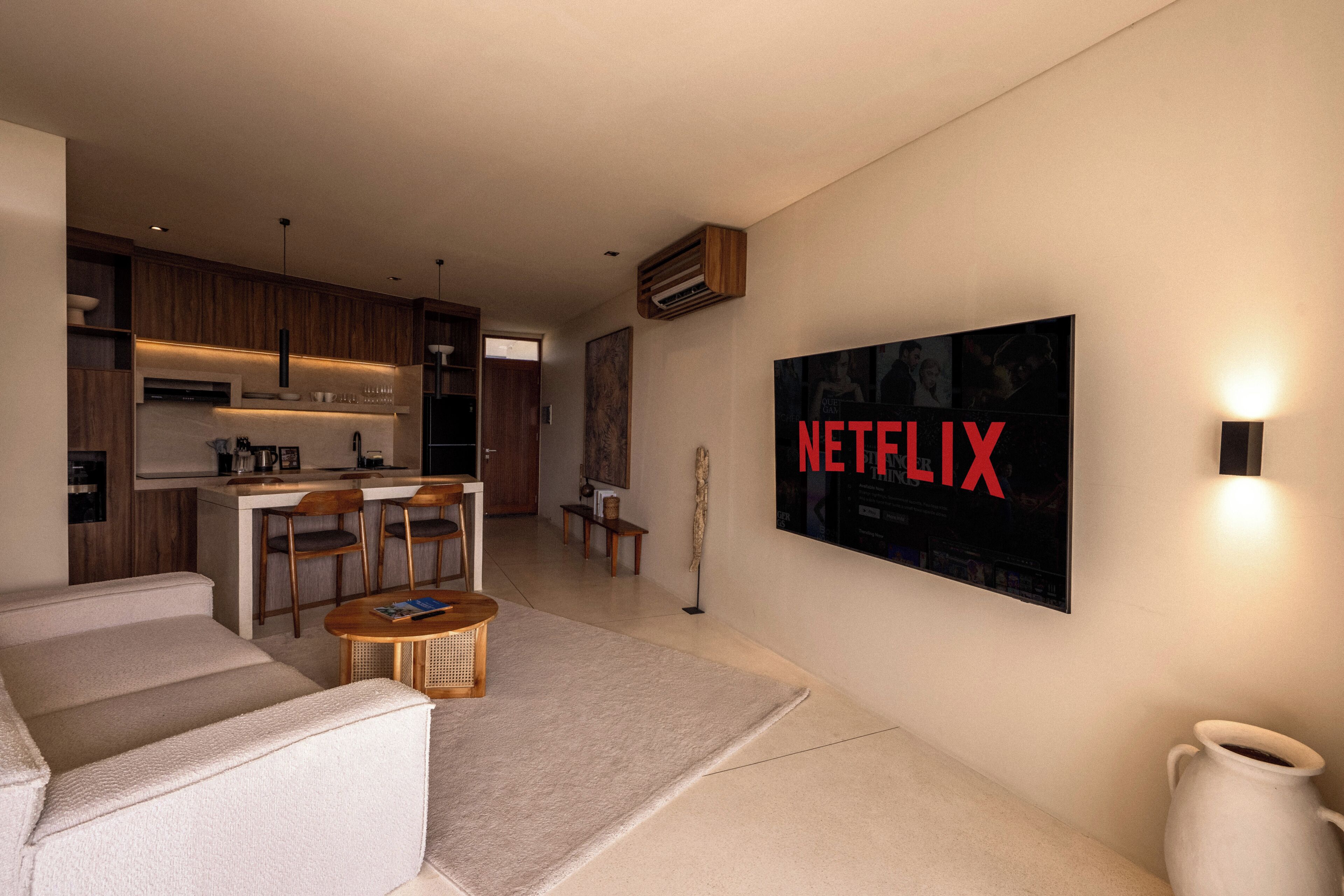 A modern living room with a sofa, a coffee table, and a TV mounted on the wall displaying 'NETFLIX'.
