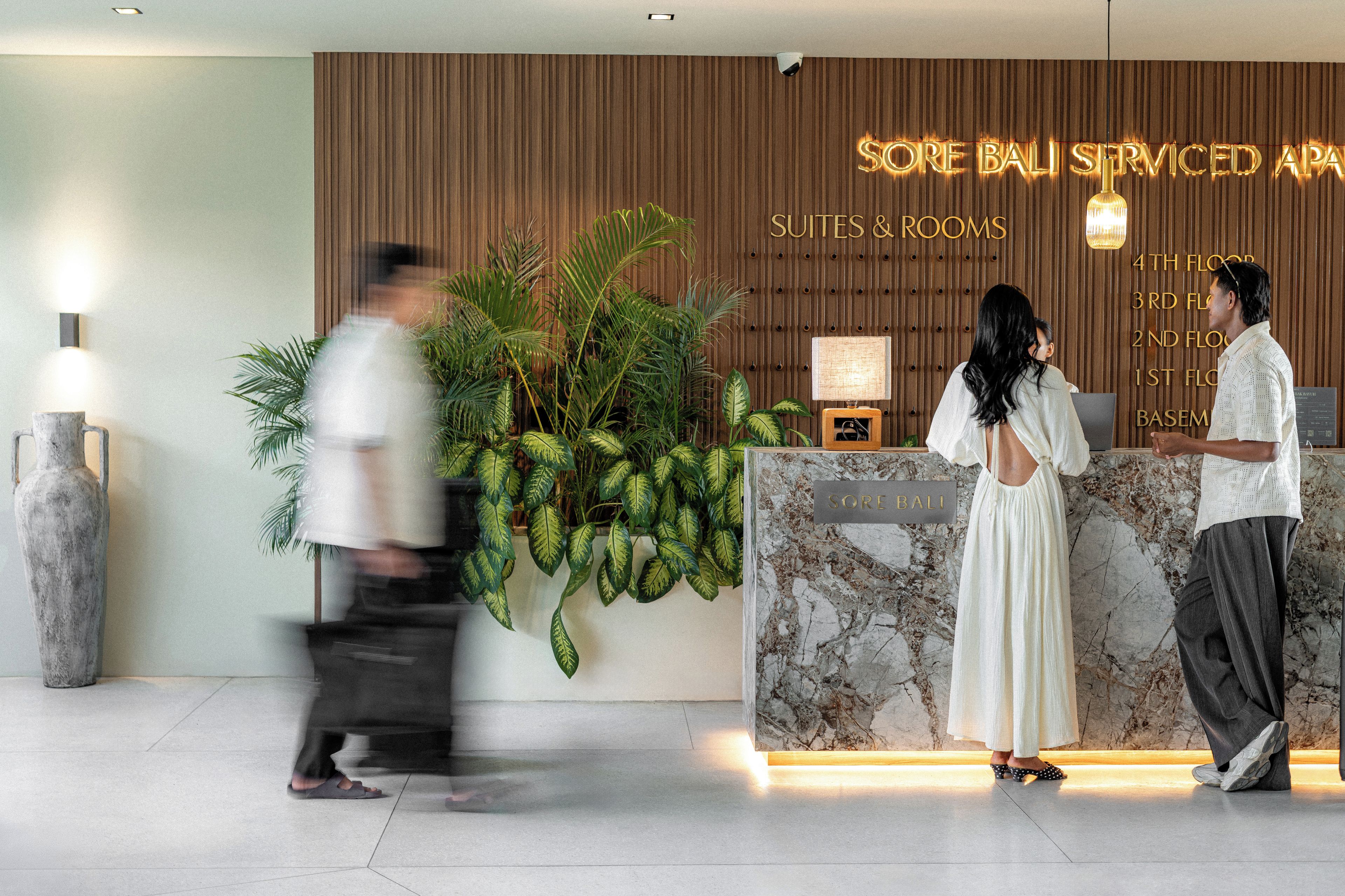 A reception desk with a sign indicating 'Sore Bali Serviced Apartments' and a list of floors.