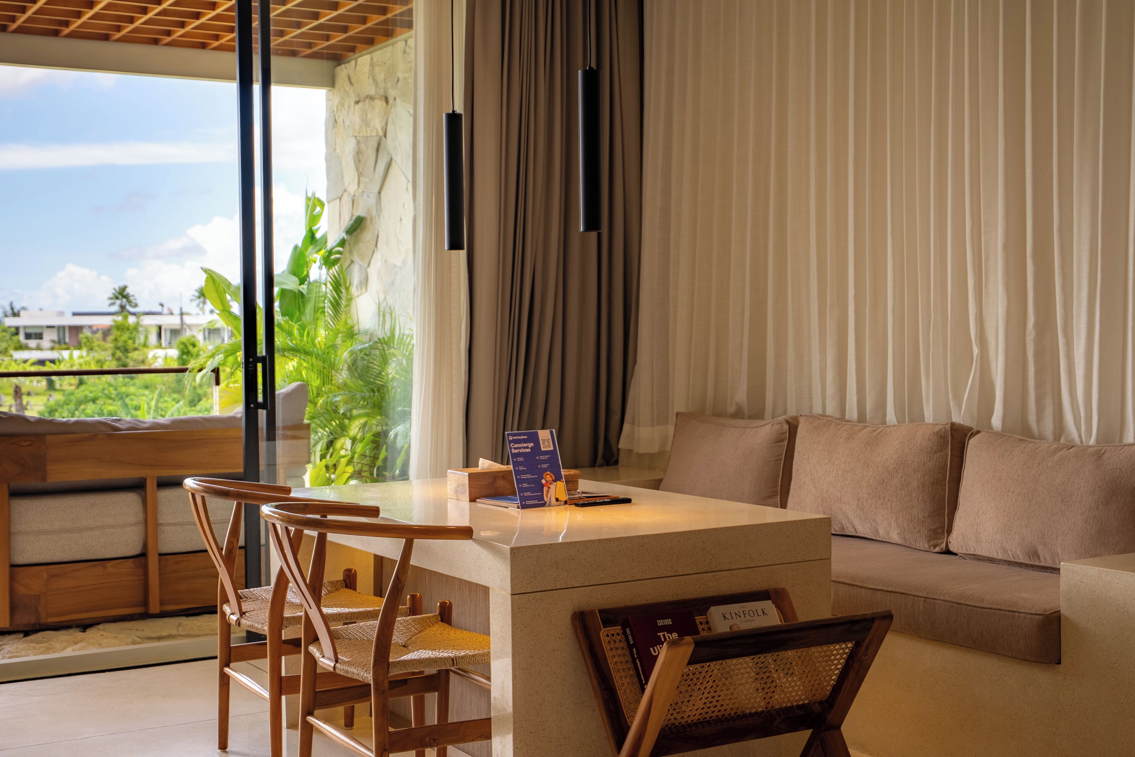 A modern living room with a sofa, a dining table with chairs, a view of the outdoors, and a stone wall.