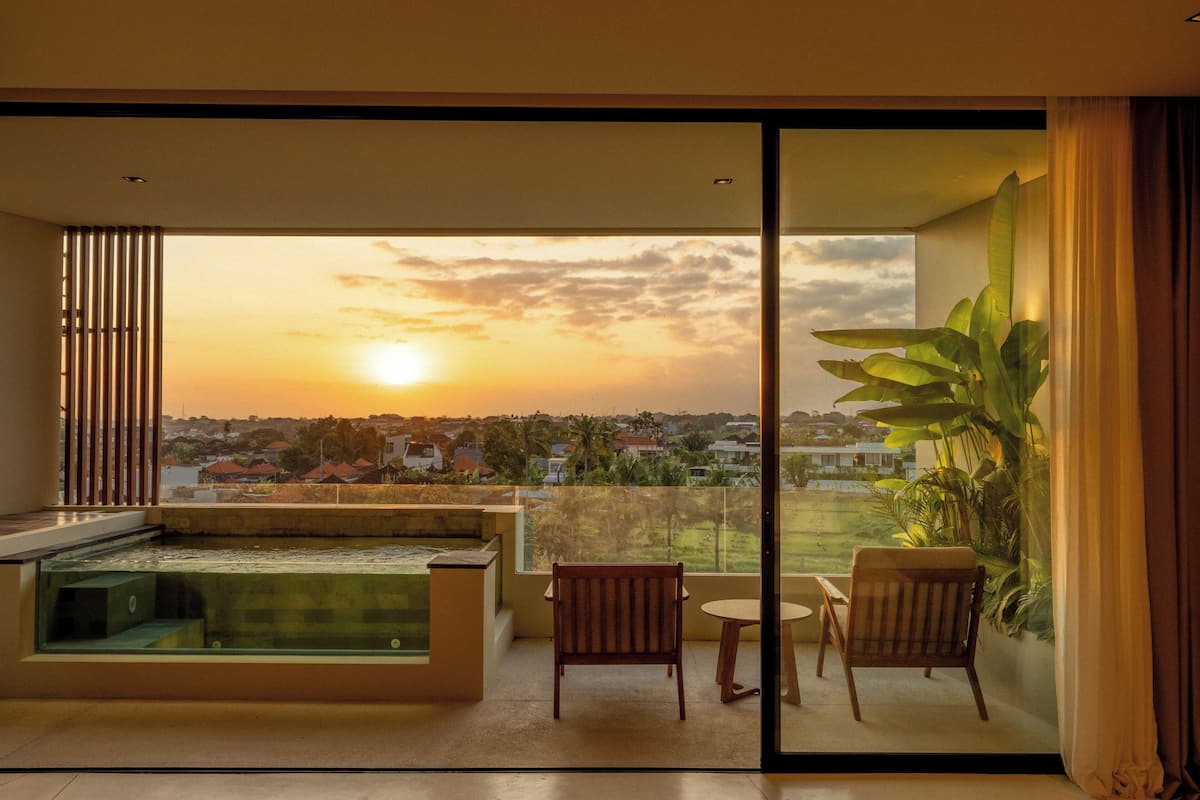 Ein Balkon mit Whirlpool, zwei Stühlen und Blick auf den Sonnenuntergang über einer Wohngegend.