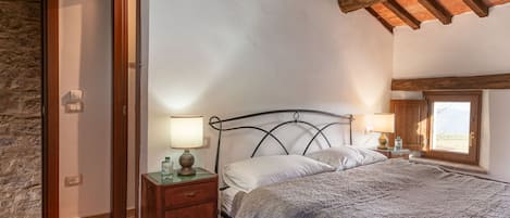 A bedroom with a bed, bedside tables, a lamp, a window, and a stone wall.