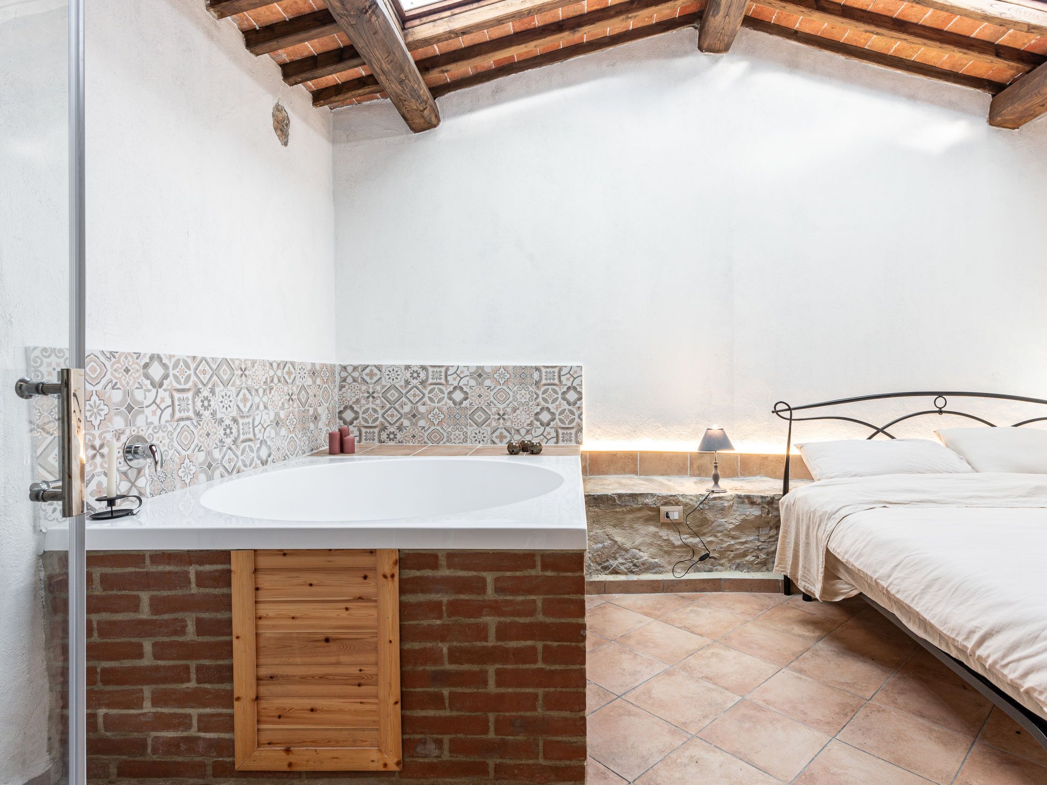 Een badkamer met een groot bad, een houten kast, een betegelde muur, een bakstenen muur en een bed met een witte spreidekker.