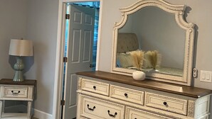 Una habitación con un aparador blanco, un espejo, una lámpara y una puerta que da a otra estancia.