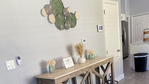 Una consola de madera con platos decorativos y un letrero, una cesta colgante negra y una puerta en un pasillo con piso gris.