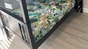 Una cama litera con una funda de colchón con motivos de selva, un cojín con diseño similar y una estructura metálica.