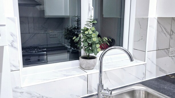 Une cuisine moderne dotée d’un évier en acier inoxydable, d’une fenêtre donnant sur l’intérieur et d’une plante en pot posée sur le rebord de la fenêtre.