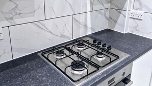 Une cuisine équipée d’une cuisinière à gaz, de meubles blancs et de carreaux de marbre.