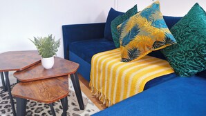 Un canapé bleu avec un plaid rayé jaune et blanc, une petite plante verte posée sur une table d’appoint en bois, et des coussins à motifs verts.