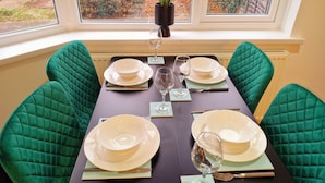 Une table à manger dressée pour quatre personnes, avec des chaises à revêtement vert, des assiettes blanches et des verres à vin.