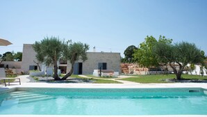 A modern poolside area with a clear blue pool, a white building with a door, and trees. - Tower House in Puglia With Pool (Cisternino)