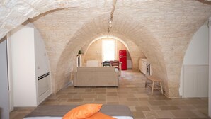 A cozy room with a stone vaulted ceiling, a bed with an orange pillow, a small table, and a red cabinet. - Tower House in Puglia With Pool (Cisternino)