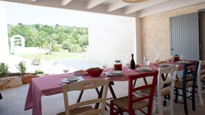 An outdoor dining area with a table set for a meal, surrounded by chairs, and a view of a garden and trees. - Tower House in Puglia With Pool (Cisternino)