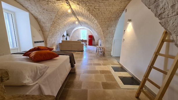 A bedroom with a stone ceiling, a bed with white bedding, an orange pillow, and a wooden ladder. - Tower House in Puglia With Pool (Cisternino)
