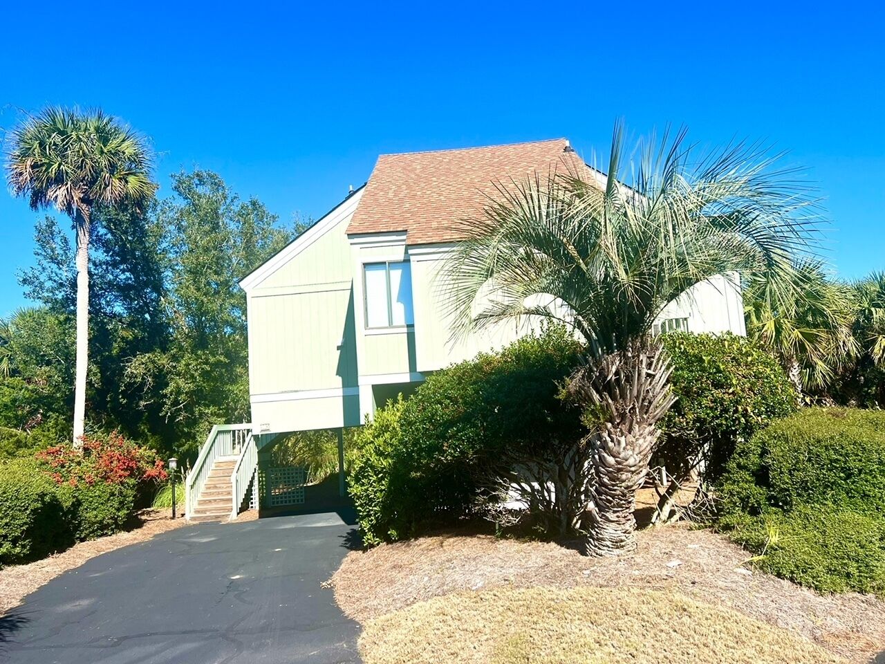 Une maison à deux étages avec une entrée à l’avant, un escalier et un palmier dans le jardin.